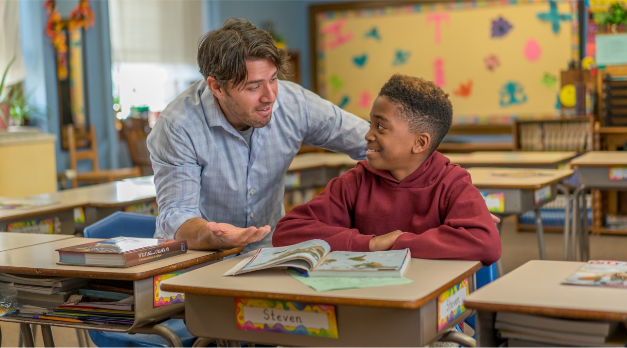 Teacher helping student named Steven learn at his desk.