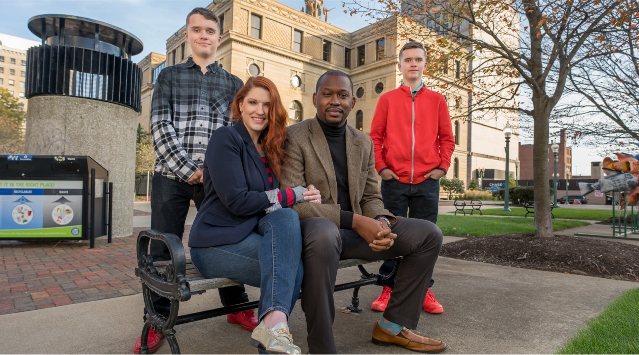 Family posing together for a picture on a park bench outside.