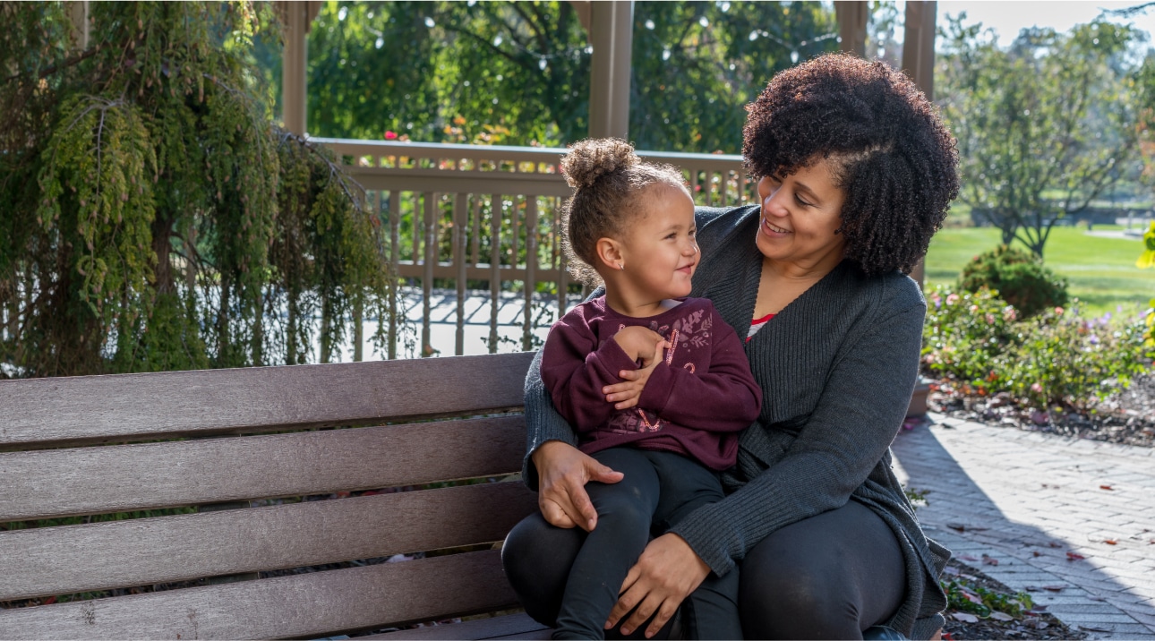 A woman and young girl sitting on a bench, smiling at each other