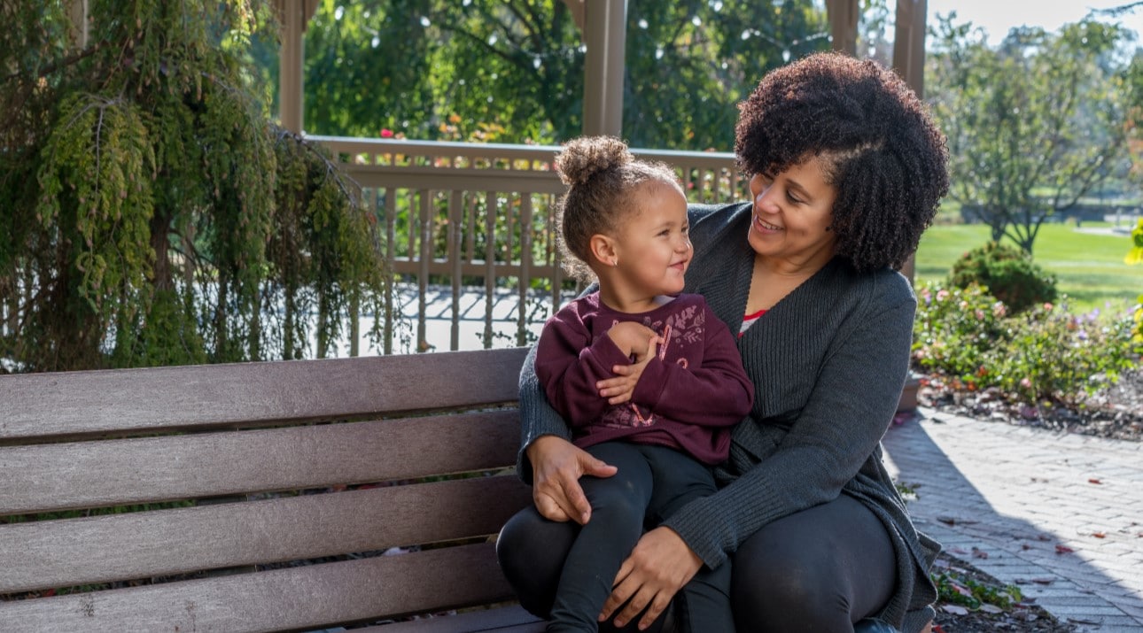 A woman and young girl sitting on a bench, smiling at each other