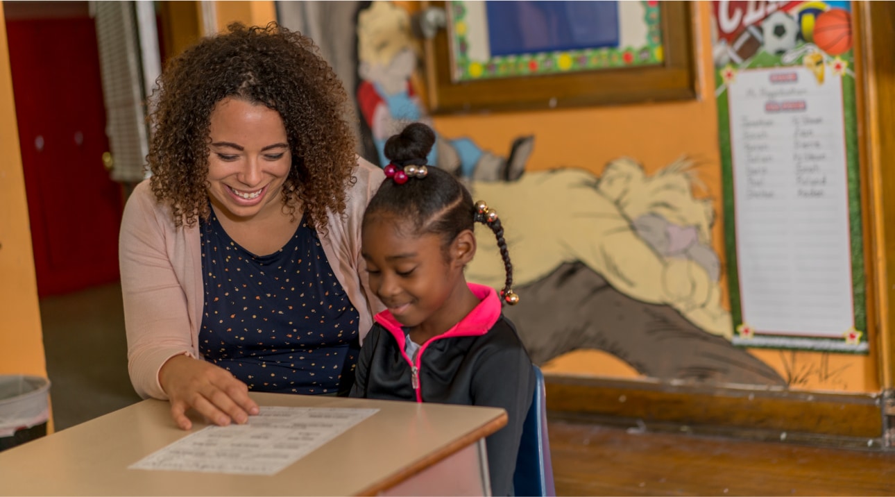 Teacher helping girl learn in school while sitting at a desk.