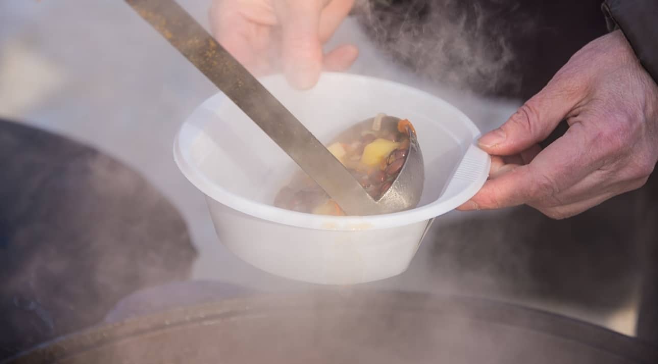 Person holding a white bowl that being filled with soup by someone else